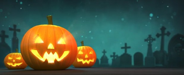 Carved pumpkins with glowing faces on a wooden surface at night with a cemetery background.